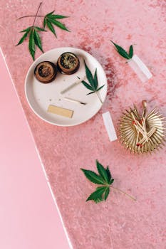 Cannabis leaves with grinders, joint, and matches on a pink velvet background.
